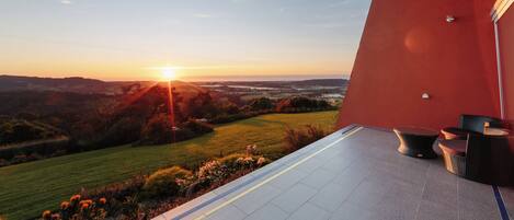 A terrace with a view of the sunset over a landscape, a red wall, and outdoor furniture.