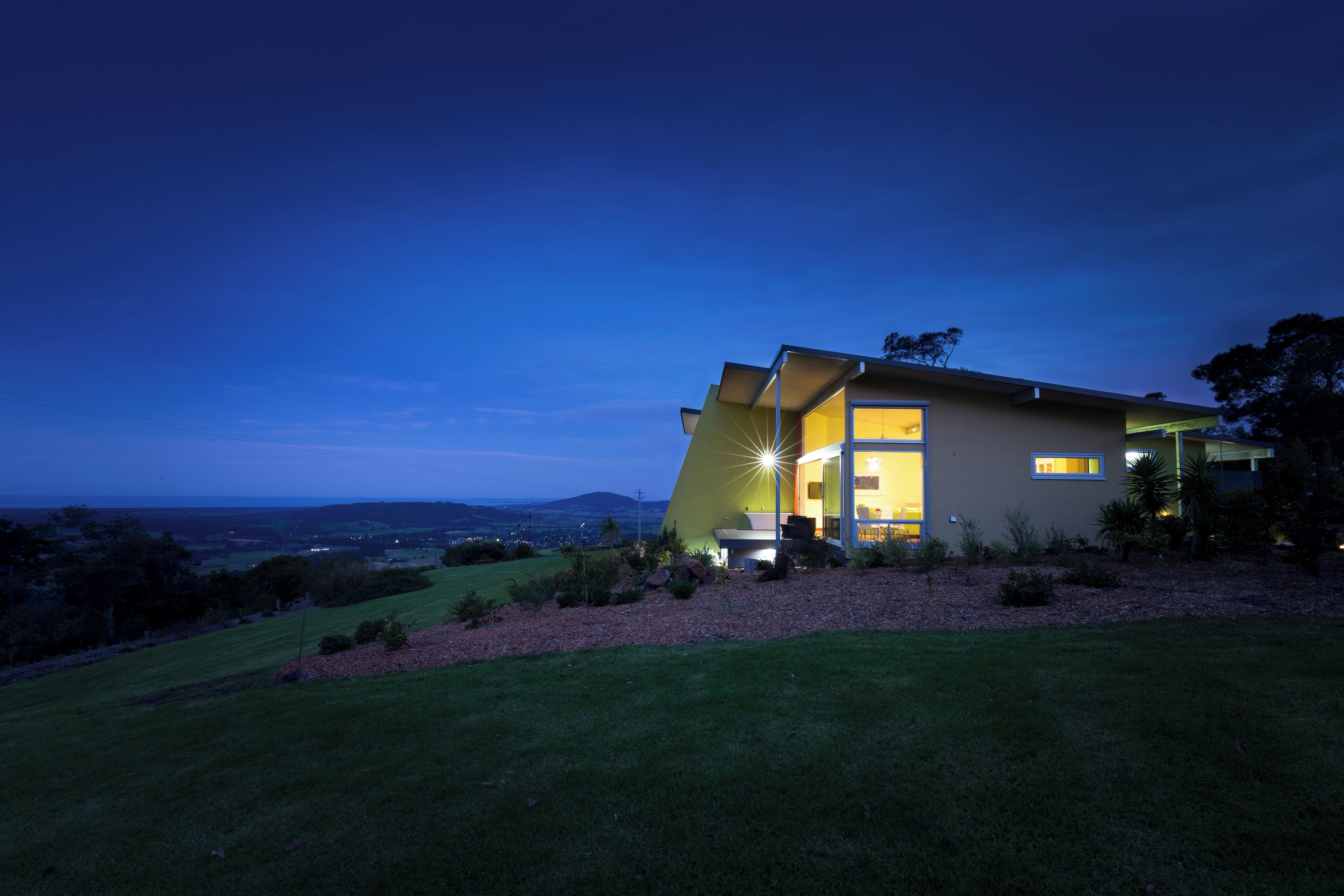 A modern house with a large glass door, surrounded by a well-maintained lawn and a view of the landscape.