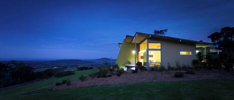 A modern house with a large glass door, surrounded by a well-maintained lawn and a view of the landscape.