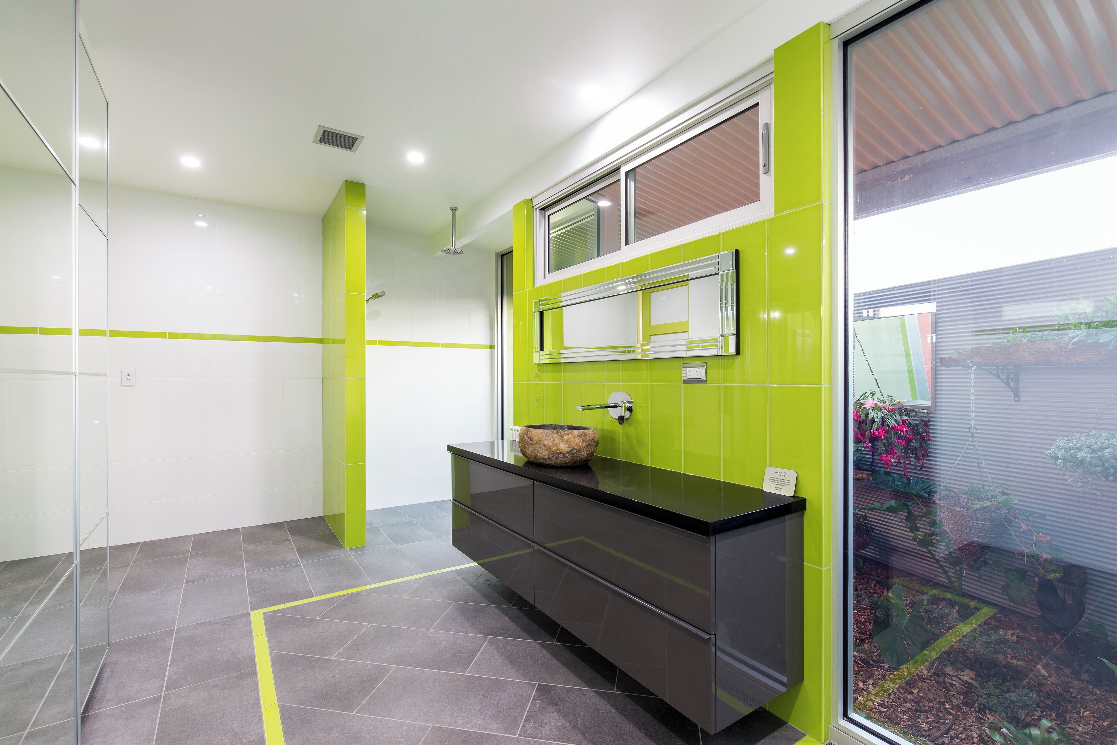 A modern bathroom with a black vanity, a green accent wall, and a large window.