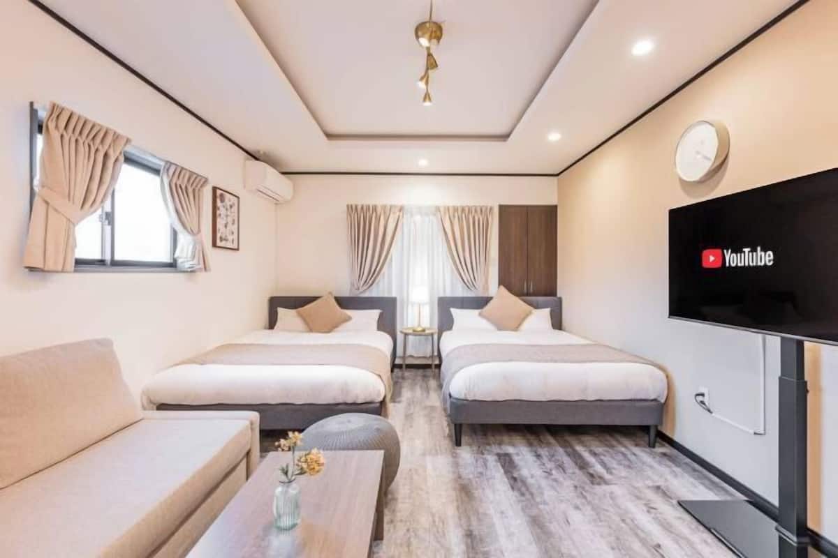 A hotel room with two beds, a sofa, a TV, and a small table with flowers.