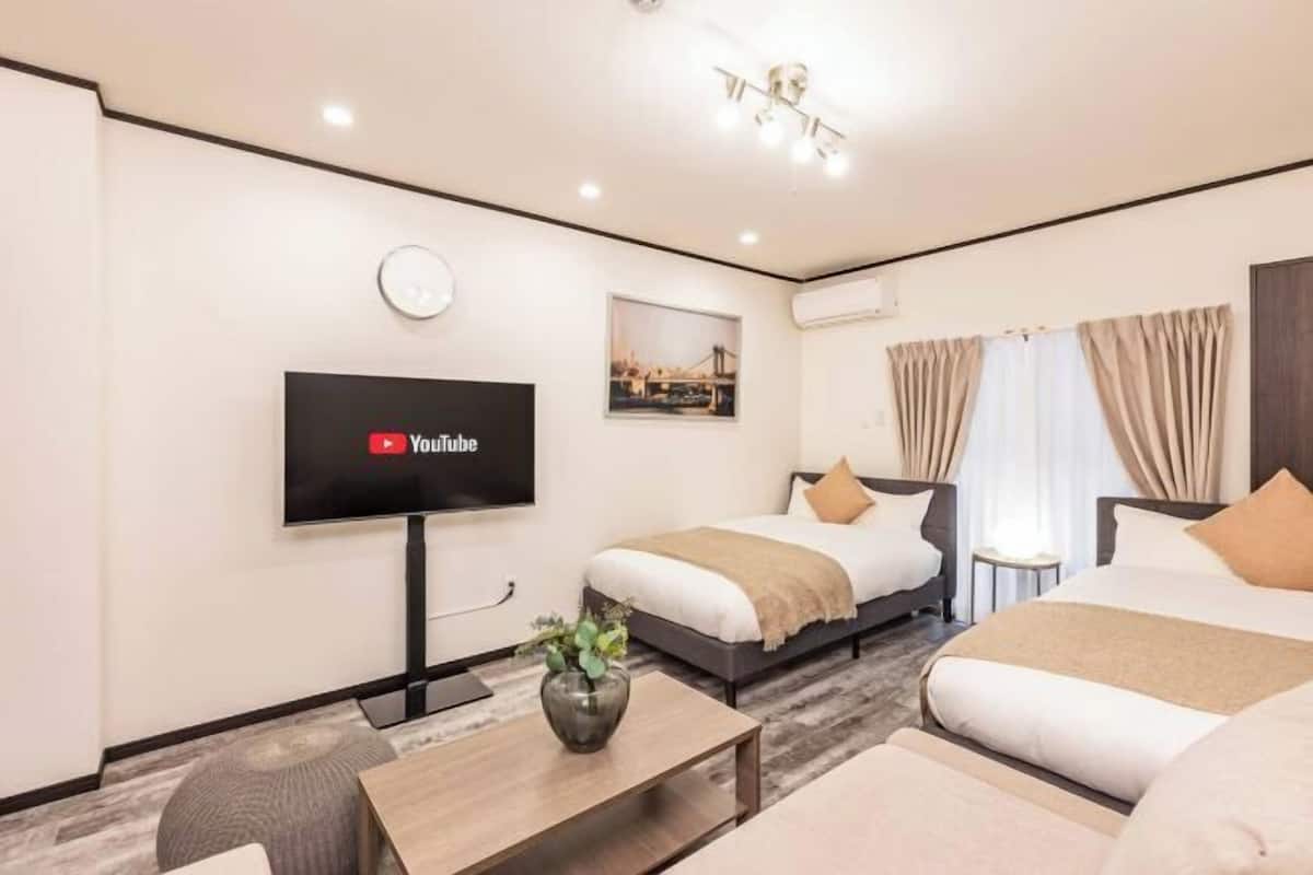 A hotel room with two beds, a TV mounted on the wall, a small table, and a window with curtains.