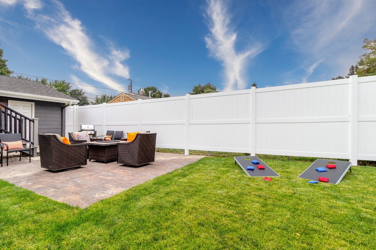 A backyard with a white fence, outdoor furniture, and shuffleboard tables.