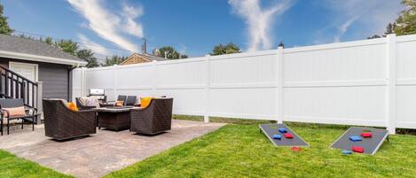 A backyard with a white fence, outdoor furniture, and shuffleboard tables.