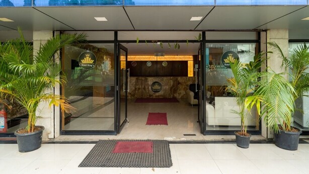 A modern hotel entrance with glass doors, a reception desk, and potted plants. - Hotel The King's (Port Blair)