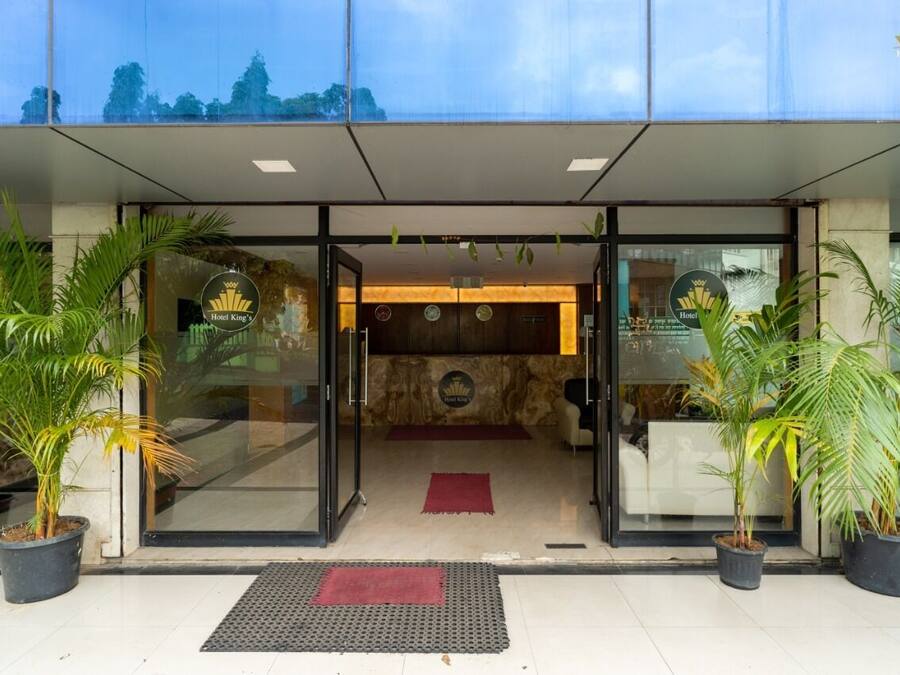 Una entrada de hotel moderna con puertas de cristal, mostrador de recepción y plantas en macetas.