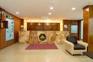 Zona de recepción de un hotel con mostrador de mármol, escritorio, cartel de recepción, un reloj y una silla.