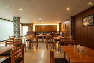 Un restaurante de hotel con mobiliario de madera, un espacio central para comer y vistas a la cocina al fondo.