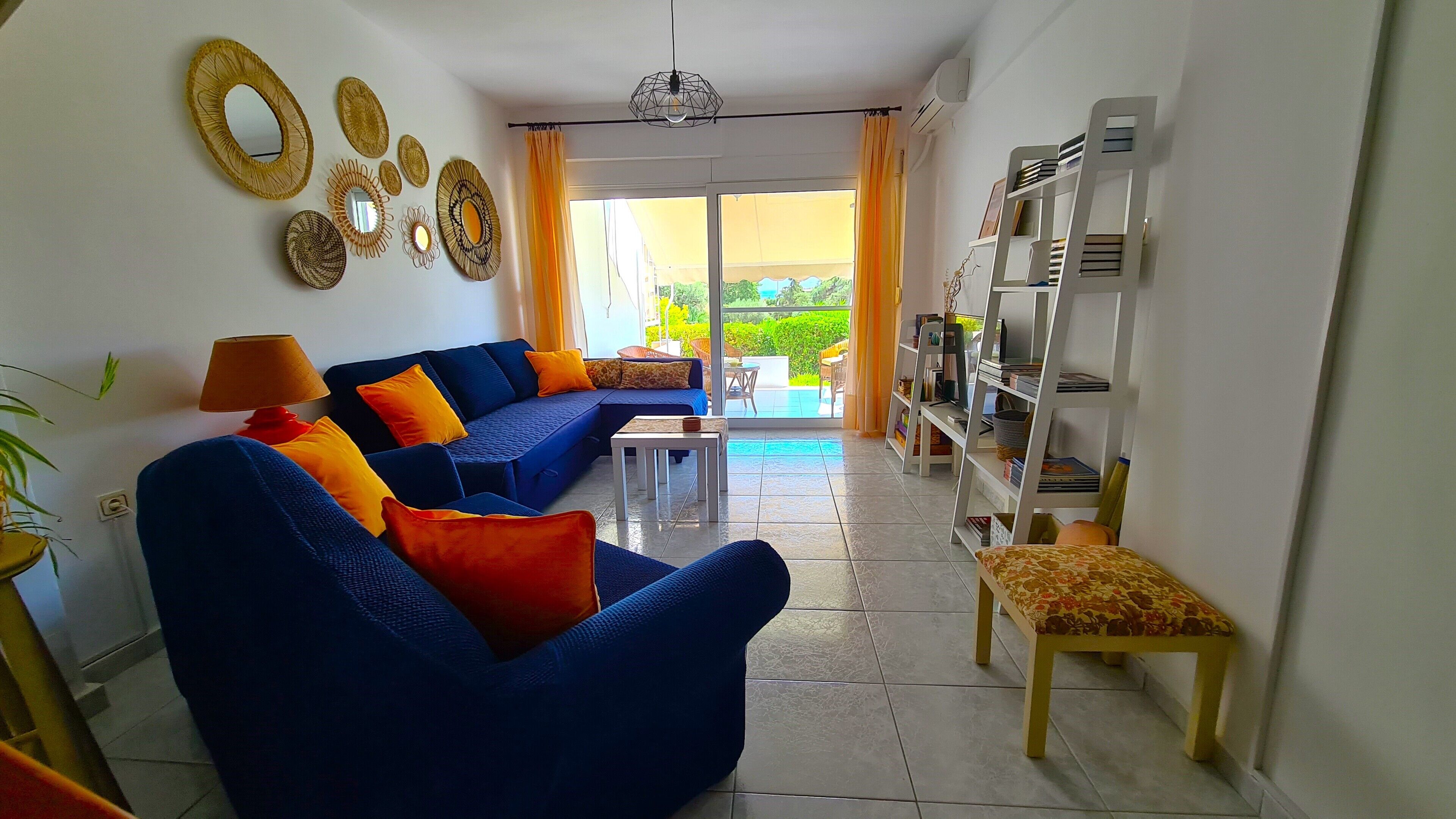 A living room with a blue sofa, orange cushions, a small table, and a bookshelf.