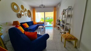 Ein Wohnzimmer mit einem blauen Sofa, orangefarbenen Kissen, einem kleinen Tisch und einem Bücherregal.
