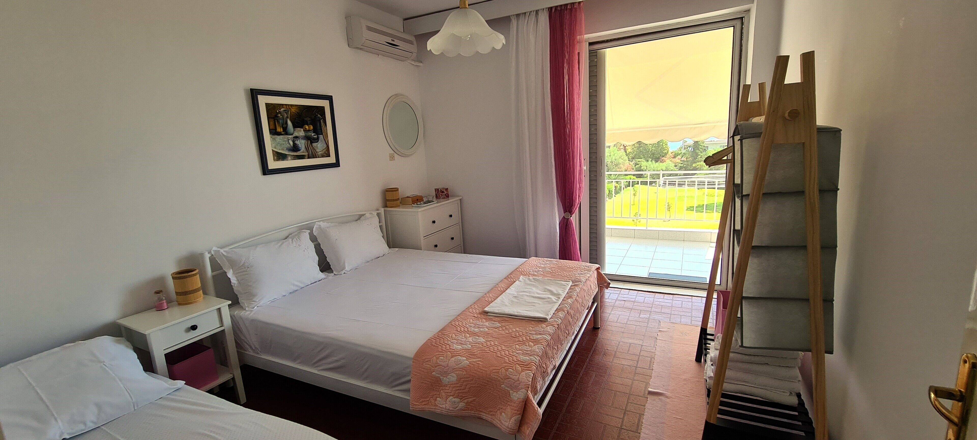 Une chambre à coucher comprenant un lit, une table de chevet, une commode, une fenêtre donnant sur un balcon et un tableau accroché au mur.