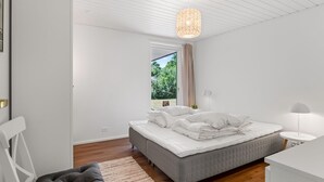 Une chambre à coucher comprenant un lit, une chaise, un bureau, une lampe suspendue et une fenêtre donnant sur un paysage verdoyant.
