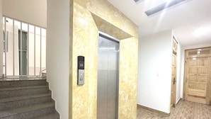 Un vestíbulo de hotel con un ascensor de mármol, una escalera y una puerta de madera.