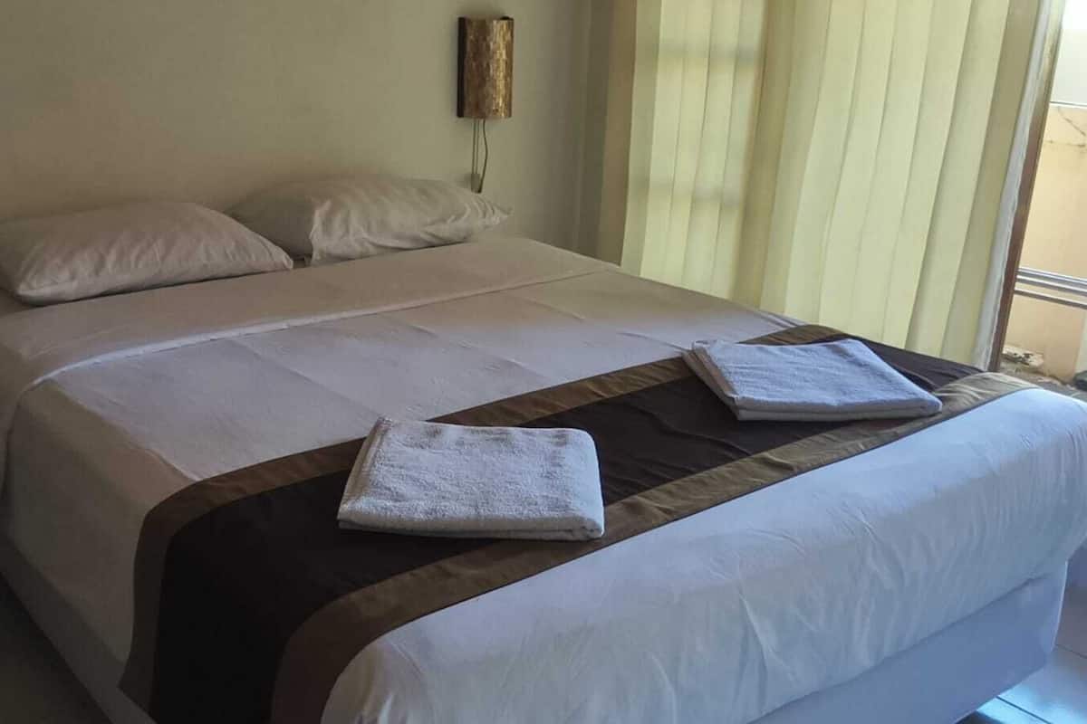 A neatly made bed with white linens and two folded towels on the bed.