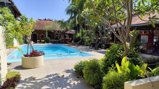 A swimming pool surrounded by lush greenery and a traditional building with a tiled roof. - Keyani's Bungalow (Sukasada)
