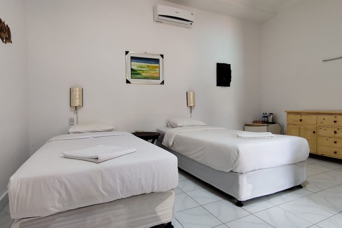 A hotel room with two single beds, a wooden dresser, a small table, and a wall-mounted air conditioner.