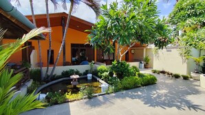 A courtyard with a small pond, potted plants, and a building with an orange facade. - Keyani's Bungalow (Sukasada)