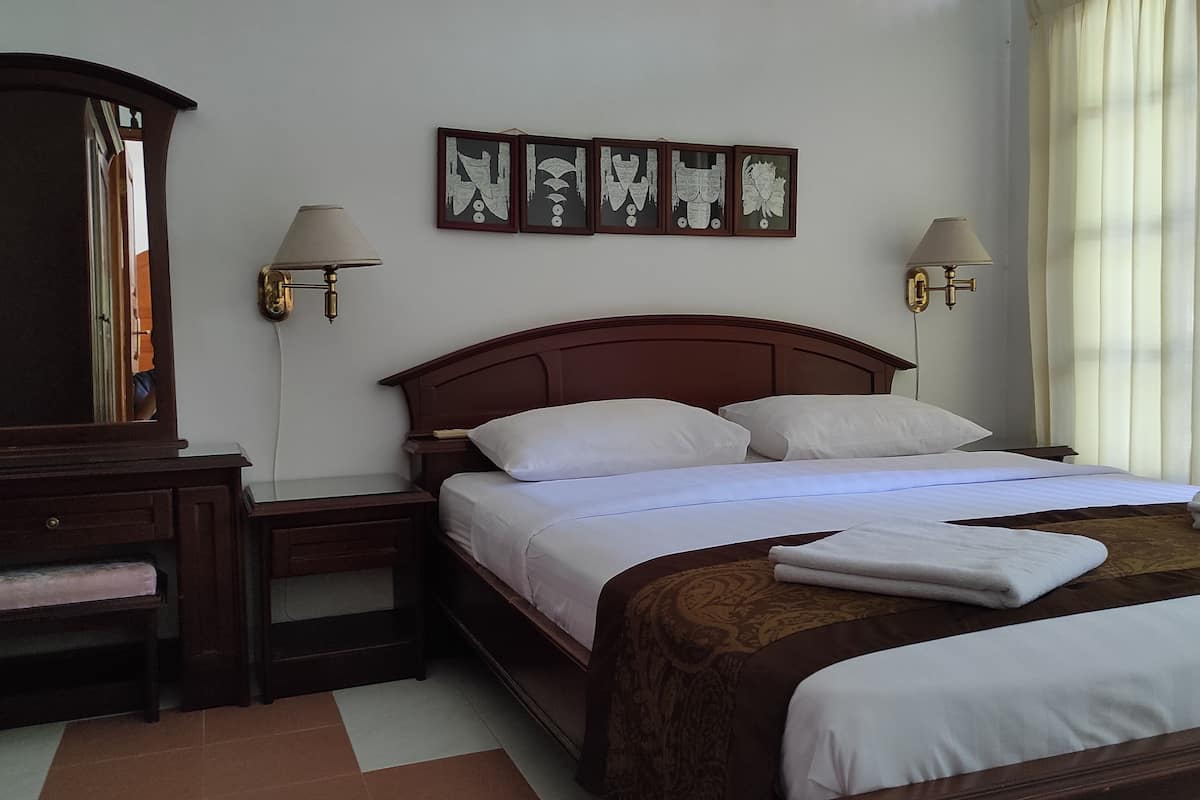 A hotel room with a wooden bed, two bedside tables, a mirror, wall-mounted lamps, and a series of framed artworks.