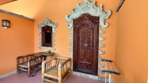 A room with an ornate wooden door, a small table with a chair, and a wall-mounted lamp. - Keyani's Bungalow (Sukasada)