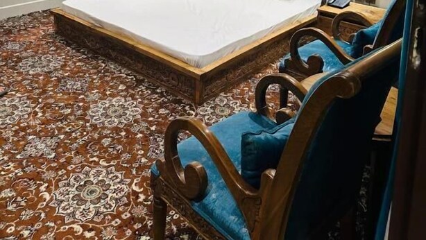 A spacious bedroom with a large bed, ornate headboard, and a patterned carpet.