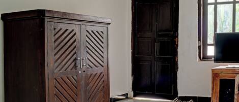 A room with a large wooden wardrobe, a closed door, and a television on a wooden stand.