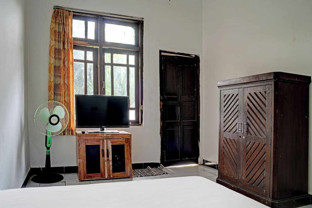 Ein Zimmer mit einem Bett, einem Fernseher auf einer Holzkommode, einem Standventilator und einem Kleiderschrank.