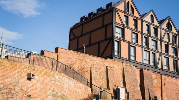 Un edificio moderno con fachada de ladrillo y ventanas amplias, destacando una sección angular con estructura metálica negra.