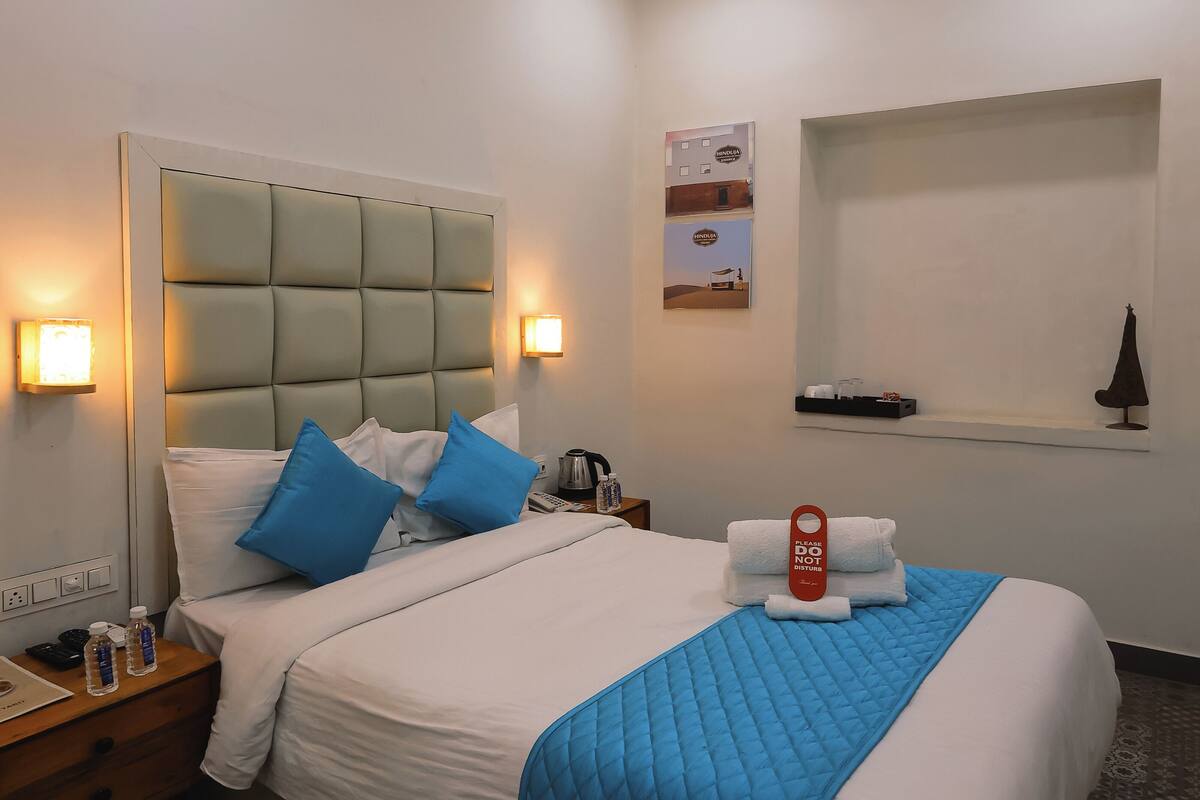 A hotel room with a bed, nightstands, a ceiling fan, wall-mounted lights, a towel rack, and a poster on the wall.