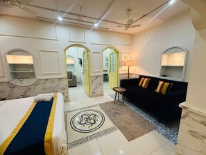 A hotel room with a bed, a black sofa, a small table, and a patterned rug. - Hinduja Haveli  (Jodhpur)