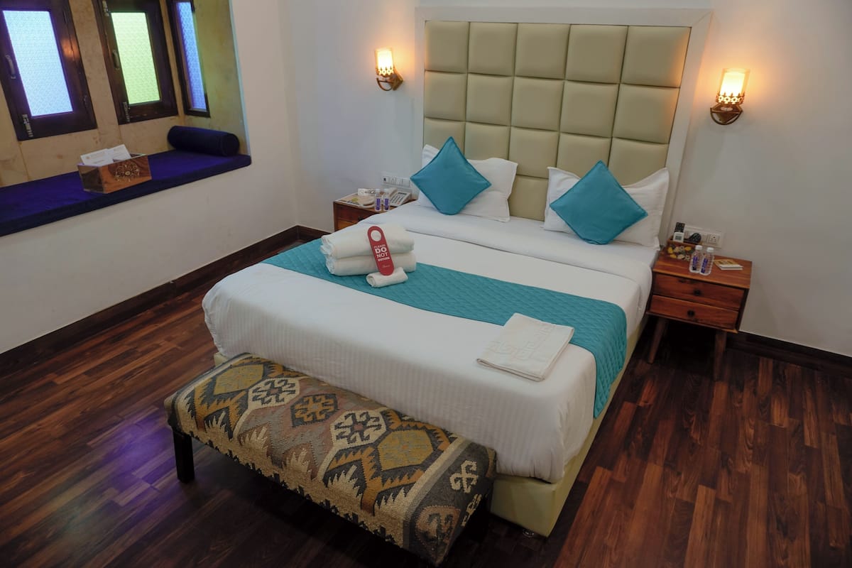 A neatly arranged hotel room with a large bed, a bench, and a small seating area by the window.