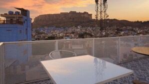 A rooftop terrace with a white table and chairs, overlooking a cityscape with a prominent hill and a building in the background. - Hinduja Haveli  (Jodhpur)