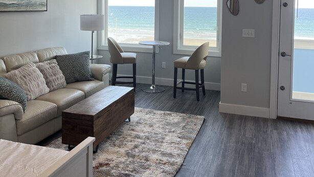 A modern living room with a view of the ocean, a beige sofa, two chairs, a coffee table, and a small round table.