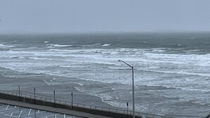 A coastal view with a paved walkway and a railing along the edge.