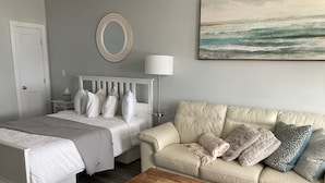 A bedroom with a bed, a nightstand, a lamp, a couch, and a wooden coffee table.