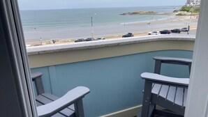 A balcony with two chairs overlooking a beach with cars and people.