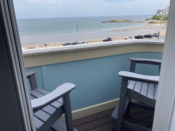 A balcony with two chairs overlooking a beach with cars and people.