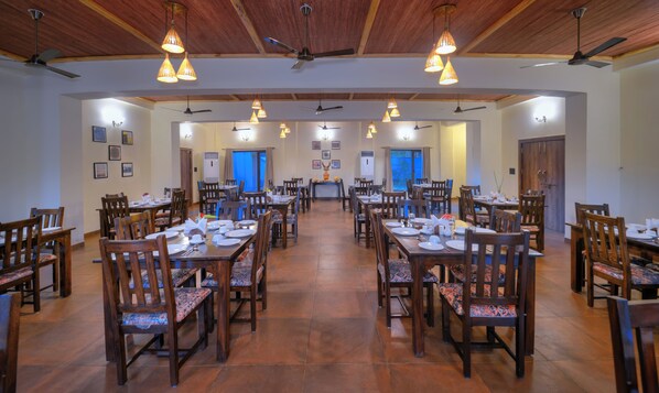 A spacious dining area with multiple tables and chairs, ceiling fans, and pendant lights.