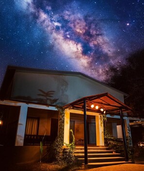 A modern house with a covered porch, steps leading up to the entrance, and a view of the night sky with stars and the Milky Way. - Aranyak Resort Kanha (Bichhiya)