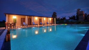 Una piscina con sillones de descanso y un edificio con ventanas iluminadas.