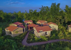 Un grupo de pequeñas casas de un piso con techos de tejas rojas, rodeadas de abundante vegetación y un cielo despejado.