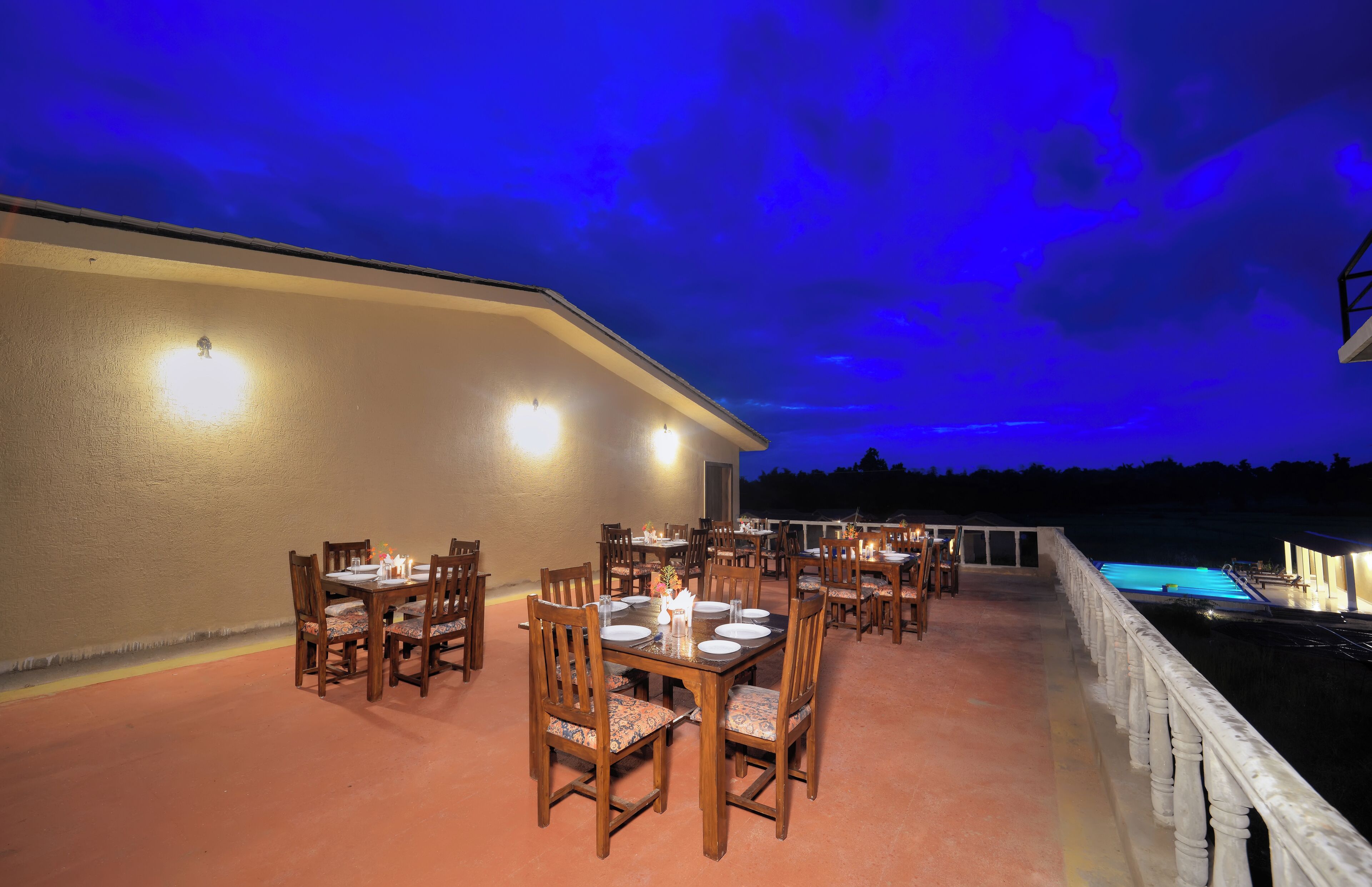 An outdoor dining area with multiple tables and chairs, a pool, and a view of the night sky.