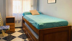 A small, neatly arranged bedroom with a single bed, a nightstand, a chair, and a window with sheer curtains. - Comeback Torrenueva Costa (Torrenueva Costa)