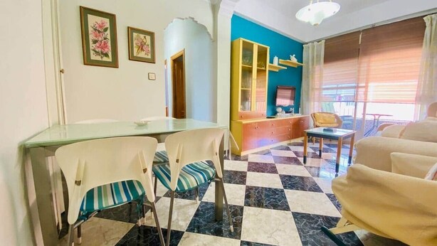 A dining area with a glass table and chairs, a blue wall, a yellow cabinet, and a checkered floor. - Comeback Torrenueva Costa (Torrenueva Costa)
