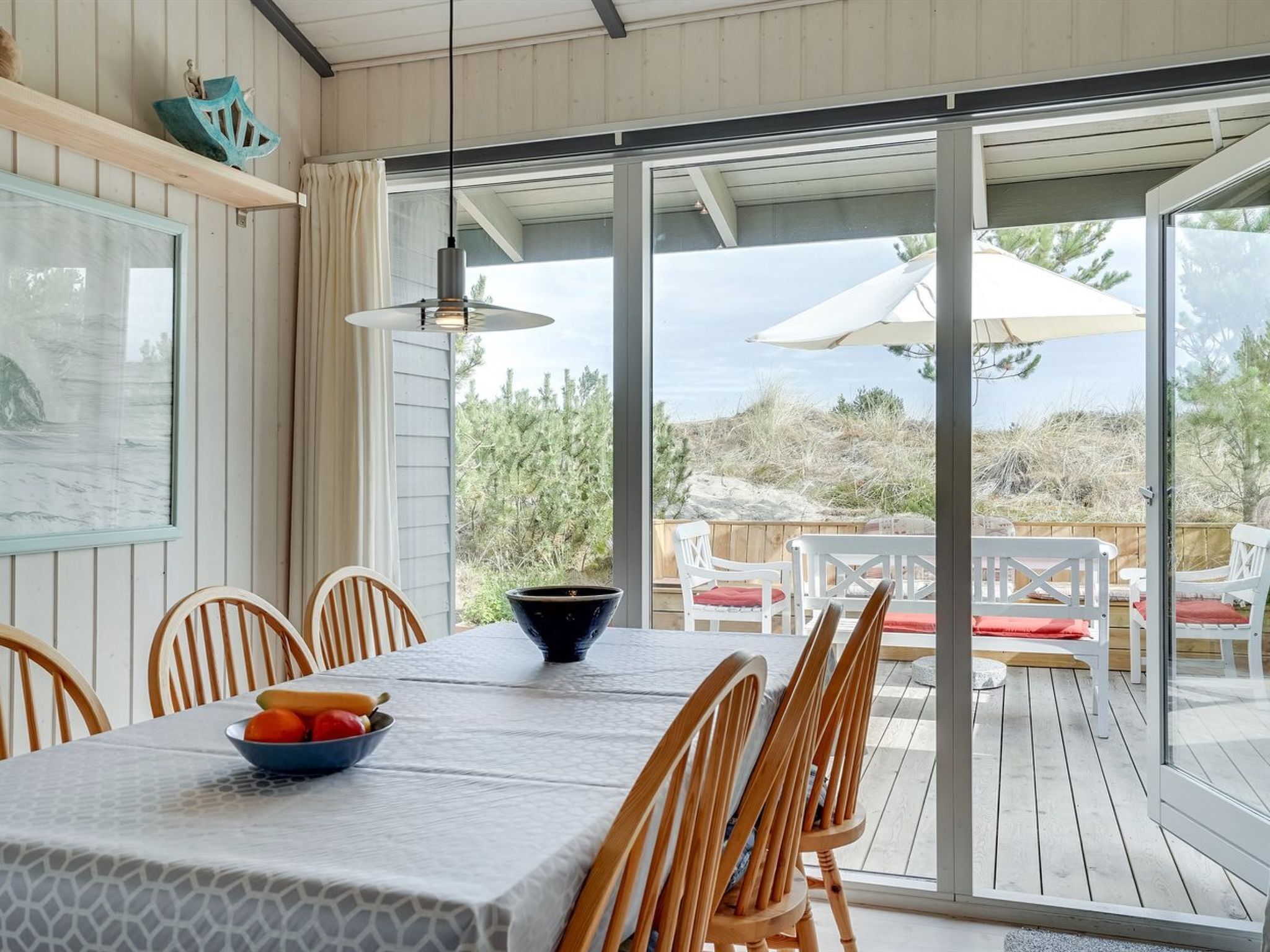 A dining area with a table set for four, a bowl of fruit, and a view of the outdoors through large sliding glass doors.