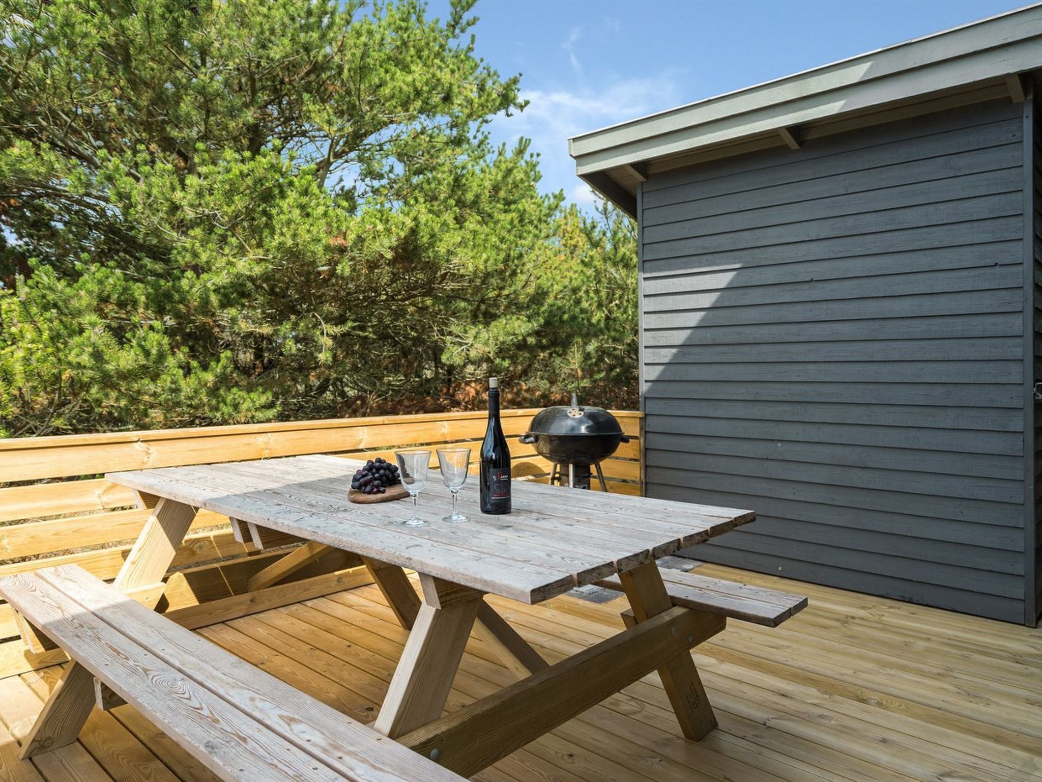 An outdoor wooden deck with a picnic table, a bottle of wine, and a grill.