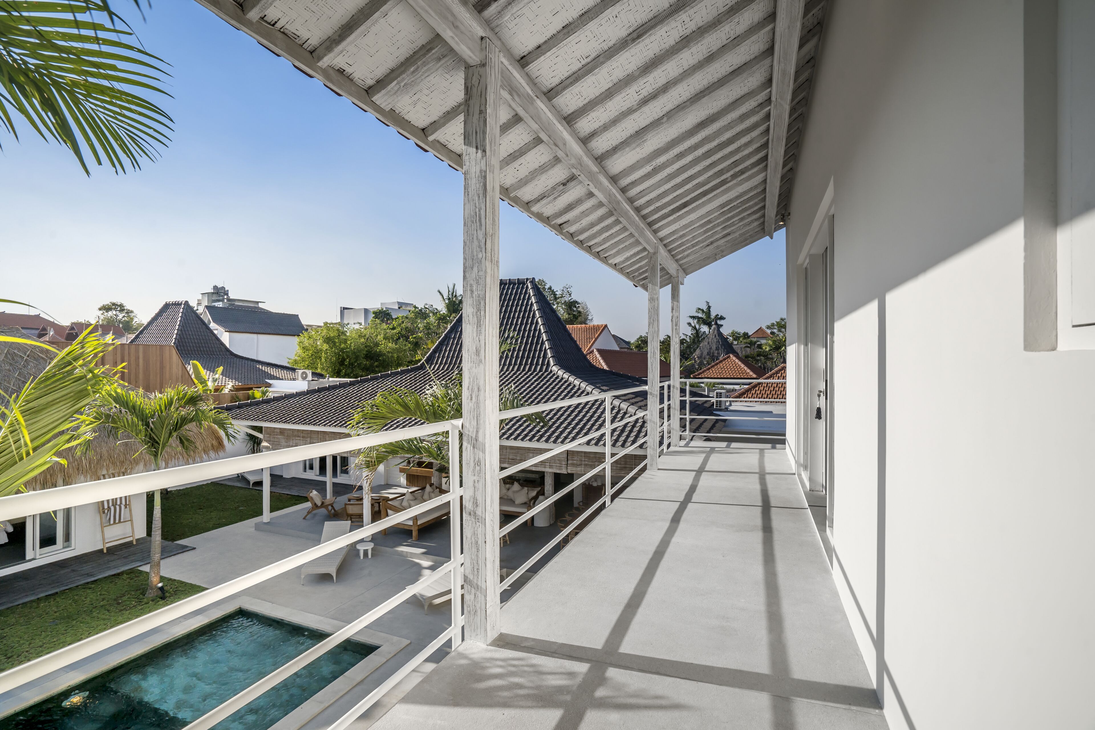 Un balcón moderno al aire libre con piscina, barandillas blancas y vistas a casas tradicionales.