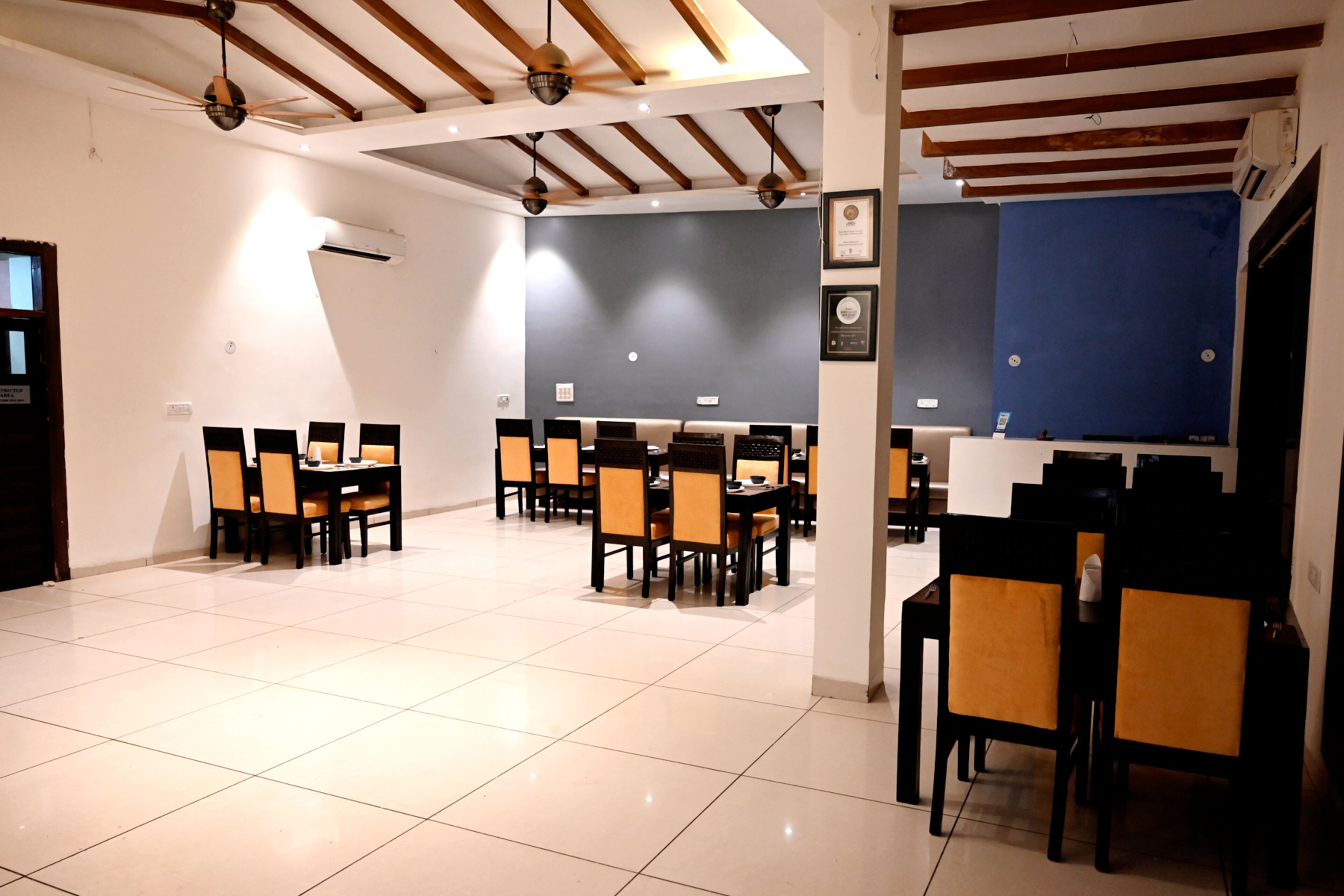 A spacious dining area with multiple tables and chairs, ceiling fans, and a tiled floor.