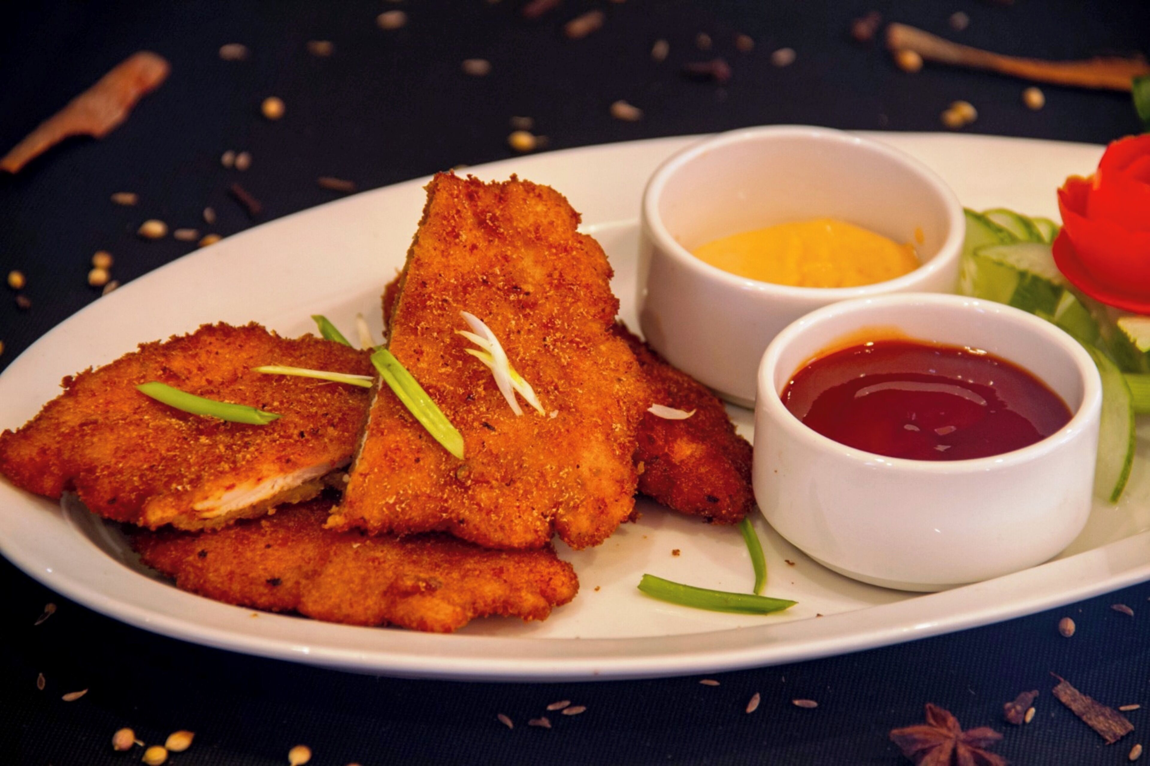 Un plato de comida empanizada y frita, acompañado de dos salsas para mojar y una guarnición de cebollines.