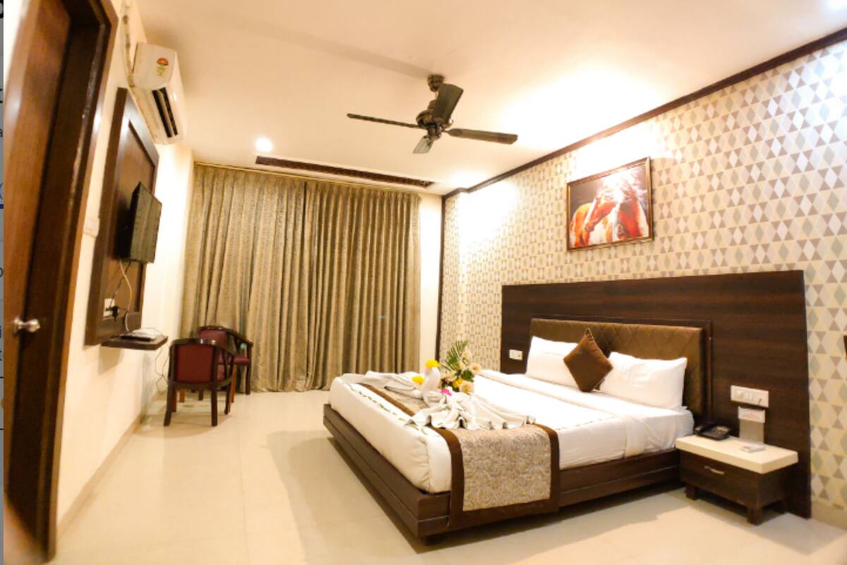 A hotel room with a bed, bedside table, nightstand, ceiling fan, and a TV mounted on the wall.