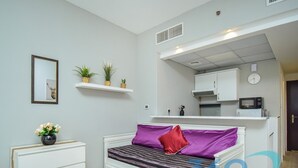 A compact living space with a bed, a small table with cups, a microwave, and a kitchenette area. - Stylish Studio in Dubai Marina Close to the Beach, Mall and Metro (Dubai)
